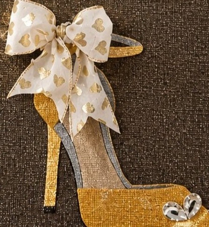 close up of Hand-painted jute tote bag featuring a gold glitter stiletto shoe on a dark background, accented with a sheer ivory bow with metallic heart details and crystal embellishments.