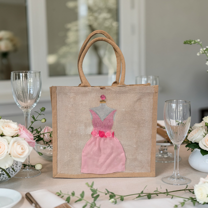 Hand-painted jute tote bag featuring a blush pink bridesmaid dress with floral details on a natural canvas background