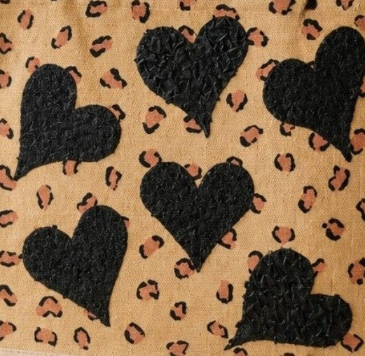 close up of Hand-painted jute shopper bag featuring textured black hearts over a tan background with scattered leopard print accents and natural tan handles.