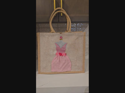 video ofHand-painted jute tote bag featuring a pink embellished cocktail dress design with floral waist details, rhinestone accents, and layered textured skirt on a natural canvas background. 