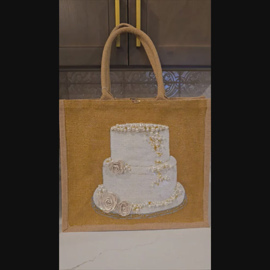 video of Hand-painted jute tote bag featuring an elegant white wedding cake with pearl and floral details on a natural canvas background