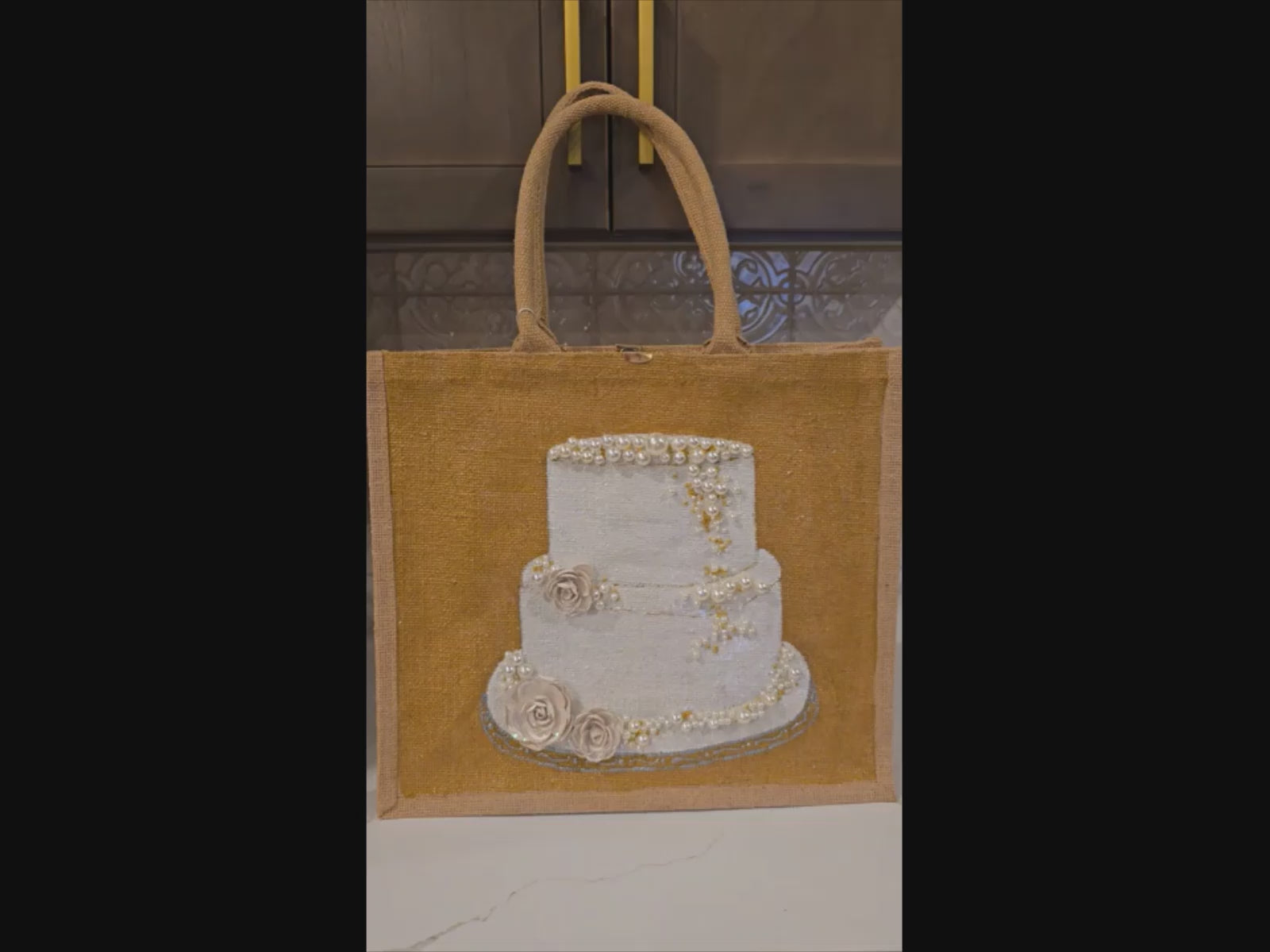 video of Hand-painted jute tote bag featuring an elegant white wedding cake with pearl and floral details on a natural canvas background