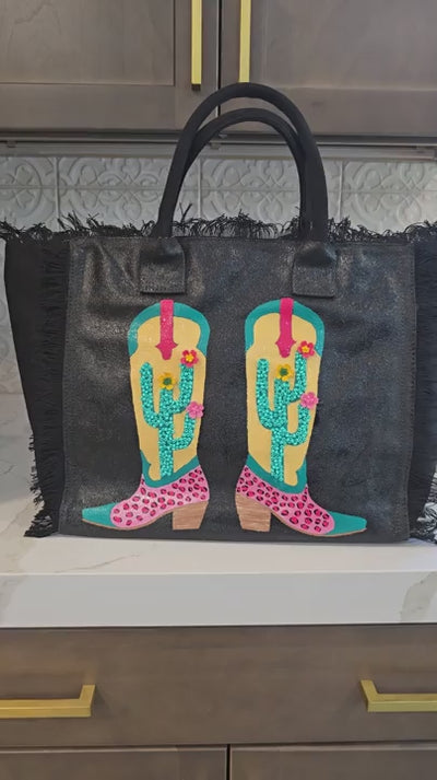 Video showcasing the Desert Kicks hand-painted Western tote bag from multiple angles, highlighting colorful cowboy boots, blooming cacti, and handcrafted embellishments.