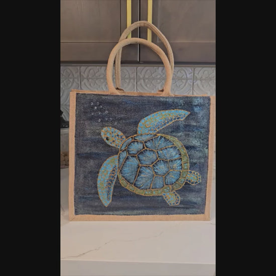 sea turtle hand-painted on burlap jute tote bag in blues, greens and golds on a navy metallic background.