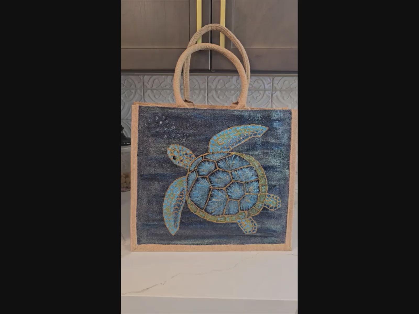 sea turtle hand-painted on burlap jute tote bag in blues, greens and golds on a navy metallic background.