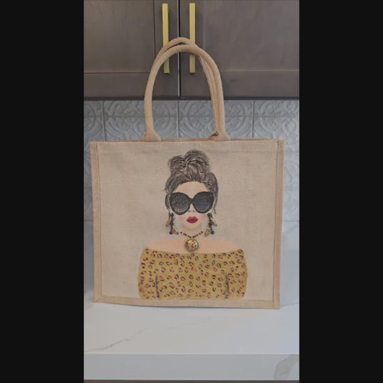 video of Hand-painted jute tote bag featuring a stylish woman with oversized black sunglasses, a leopard print off-the-shoulder top, statement earrings, and layered jewelry on a natural canvas background.