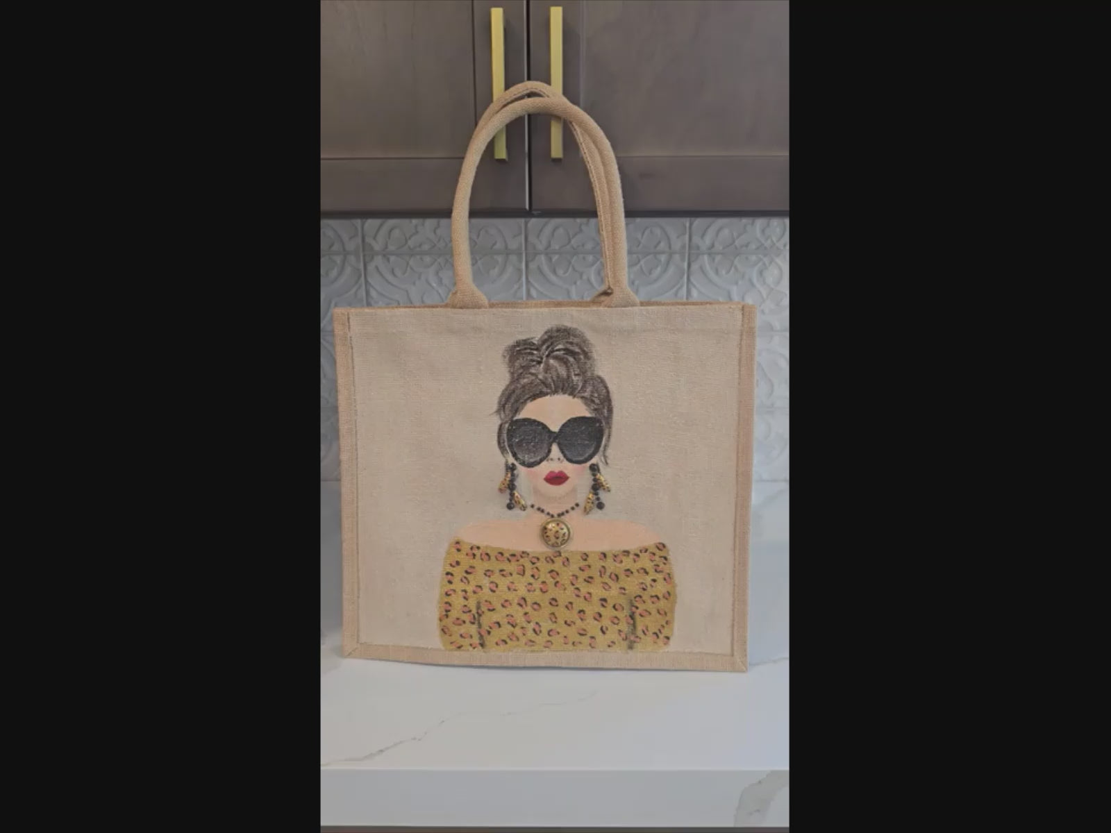 video of Hand-painted jute tote bag featuring a stylish woman with oversized black sunglasses, a leopard print off-the-shoulder top, statement earrings, and layered jewelry on a natural canvas background.