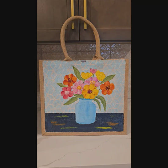 Hand-painted jute tote bag featuring colorful flowers in a blue vase against a light patterned background