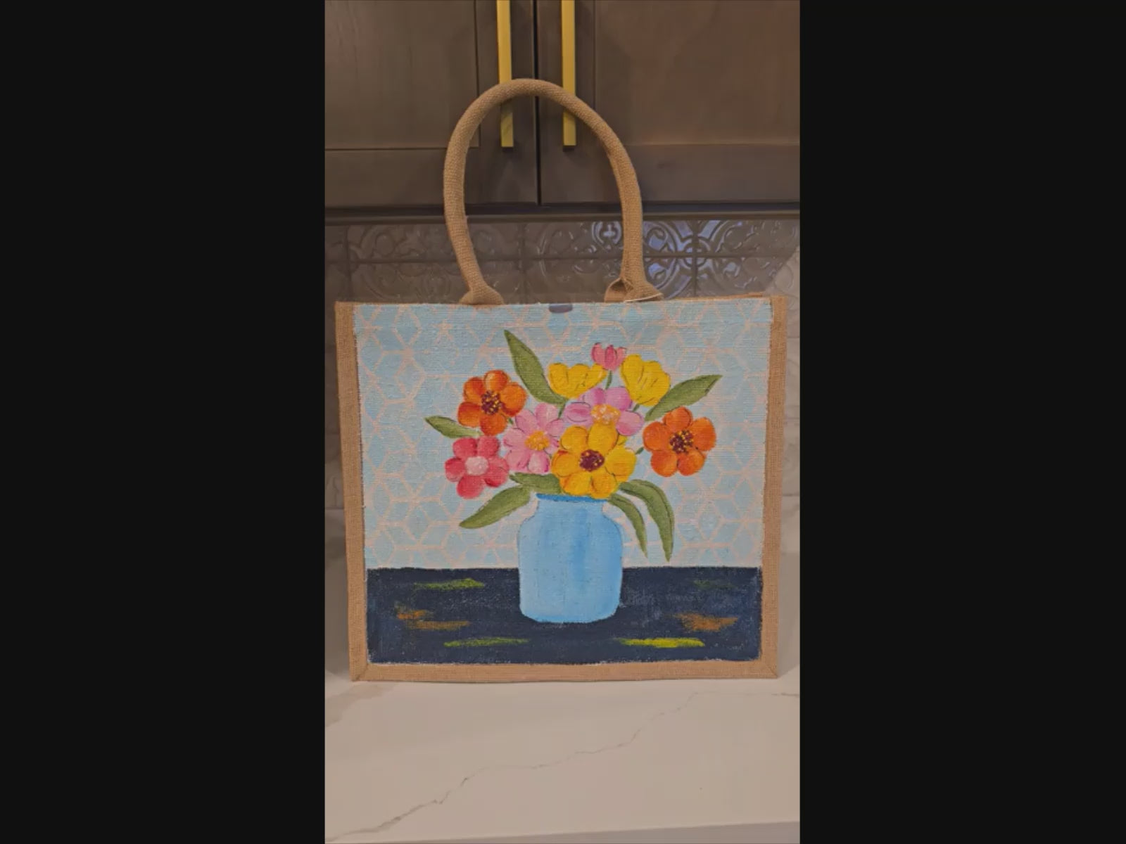 Hand-painted jute tote bag featuring colorful flowers in a blue vase against a light patterned background