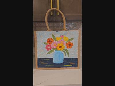 video of Hand-painted jute tote bag featuring colorful flowers in a blue vase against a light patterned background
