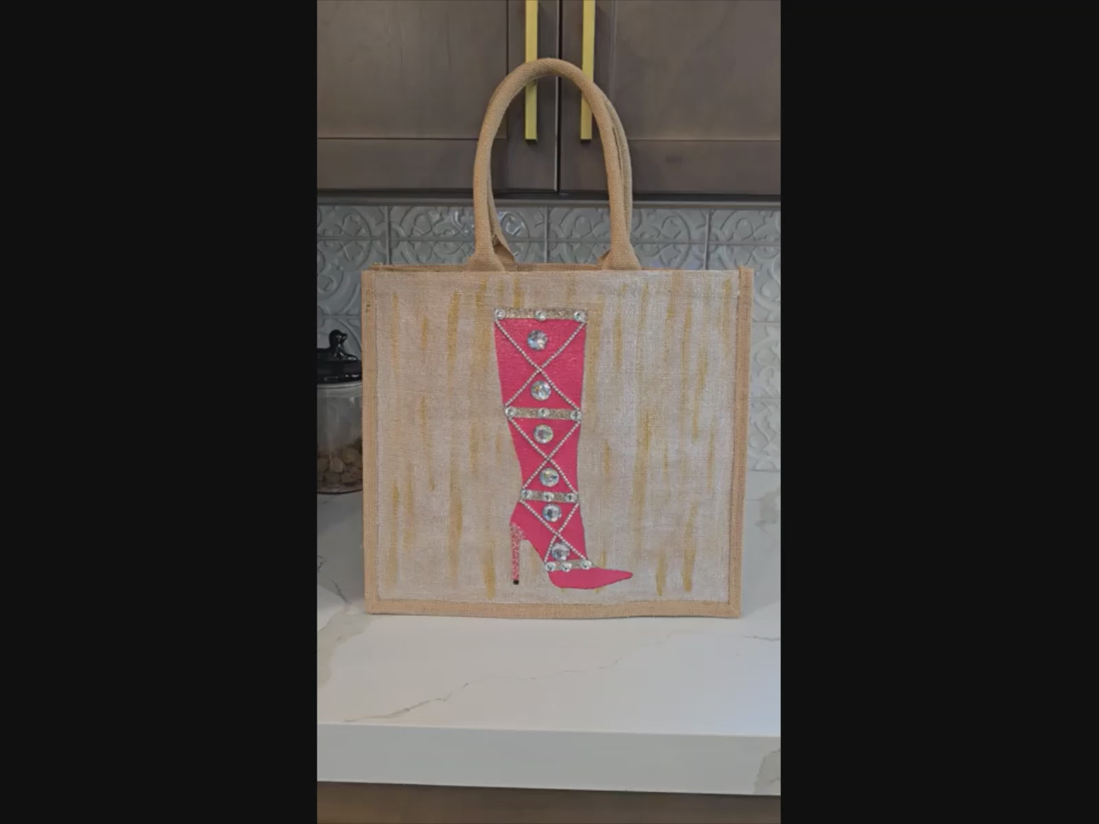 Hand-painted pink jeweled boot tote bag on a natural jute tote featuring sparkling crystal embellishments, a bright pink knee-high boot design, soft neutral background tones, and structured over-the-shoulder handles.