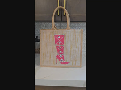 Hand-painted pink jeweled boot tote bag on a natural jute tote featuring sparkling crystal embellishments, a bright pink knee-high boot design, soft neutral background tones, and structured over-the-shoulder handles.