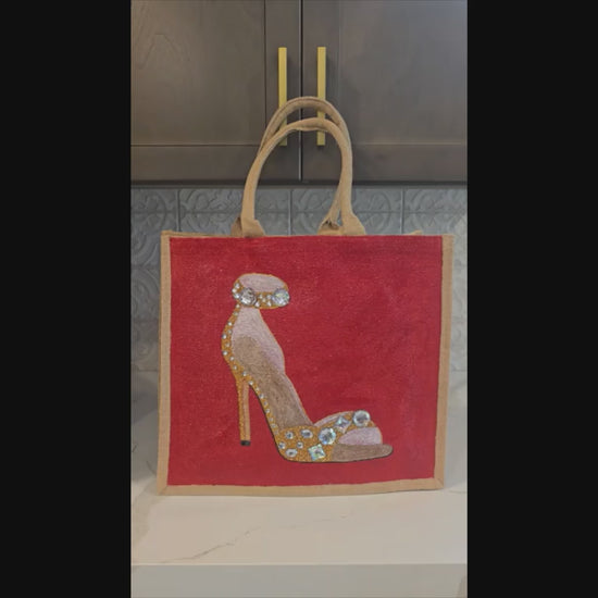 Video of Hand-painted gold stiletto tote bag with jeweled accents on natural jute background with close ups