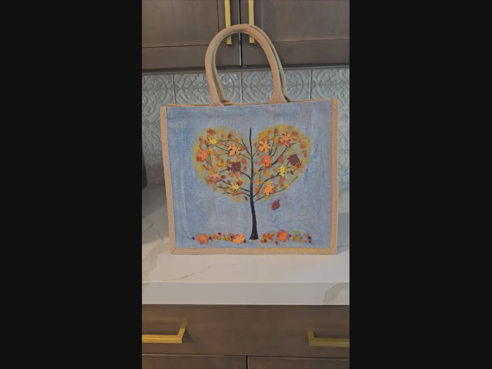 Hand-painted jute tote  featuring a heart-shaped fall tree with colorful leaves in red, orange, and gold; painted on a pale blue metallic background with beads and wooden embellishments