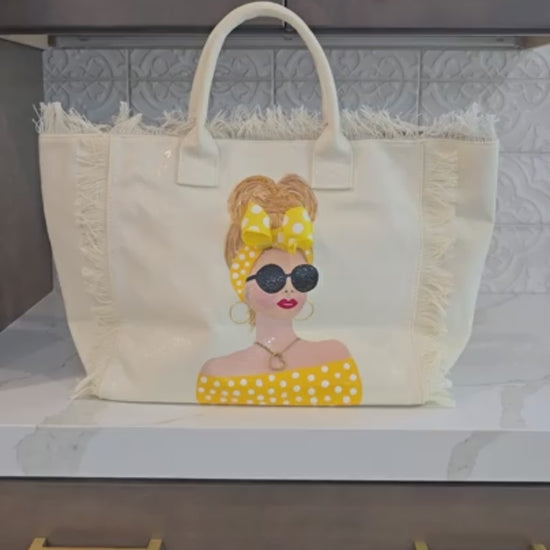 close up video of Sunshine Muse hand-painted fringed canvas tote with blonde woman in yellow polka dots and sunglasses