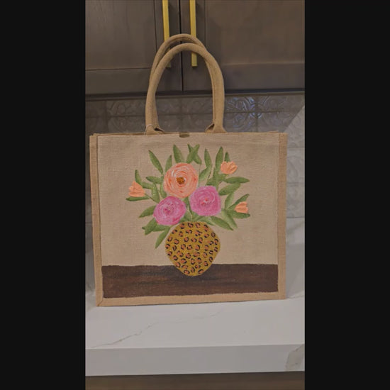 Hand-painted jute tote bag featuring pink and peach flowers arranged in a leopard print vase on a natural canvas background