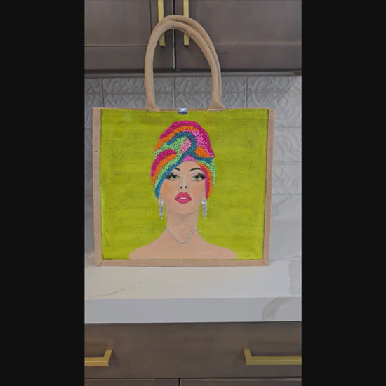 Video of Hand-painted Vivid Muse tote bag featuring a stylish woman with a colorful beaded headwrap, bold makeup, and sparkling jewelry on a vibrant green background, a unique artistic fashion statement bag.