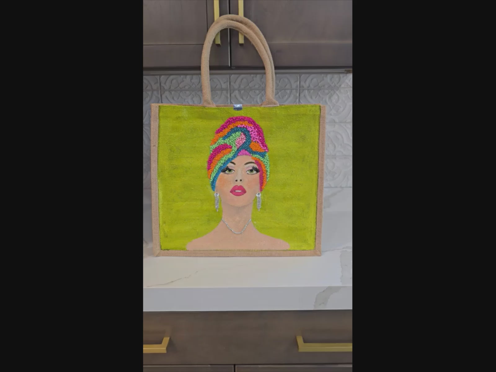 Video of Hand-painted Vivid Muse tote bag featuring a stylish woman with a colorful beaded headwrap, bold makeup, and sparkling jewelry on a vibrant green background, a unique artistic fashion statement bag.