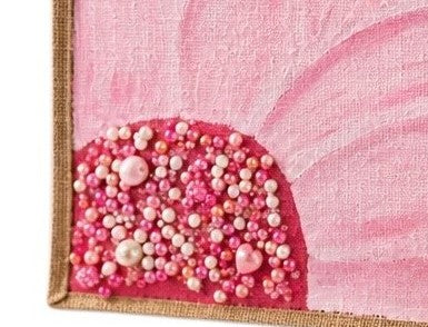Close up of Hand-painted jute tote bag featuring a large soft pink flower with layered petals and a jeweled center, accented with pearl and bead embellishments on a vibrant pink background.