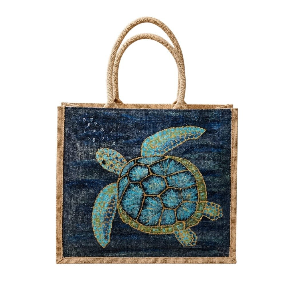 Hand-painted jute tote bag featuring a blue and turquoise sea turtle swimming underwater against a deep navy ocean background, with natural burlap handles and trim.