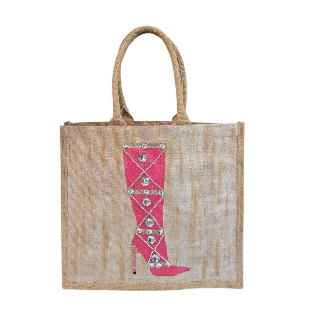 Hand-painted pink jeweled boot tote bag on a natural jute tote featuring sparkling crystal embellishments, a bright pink knee-high boot design, soft neutral background tones, and structured over-the-shoulder handles.