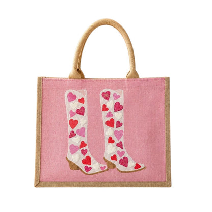 Hand-painted pink jute tote bag featuring white cowboy boots decorated with red, pink, and white heart designs. Romantic western-inspired tote bag with a soft pink background, structured handles, and Valentine-inspired wearable art details.