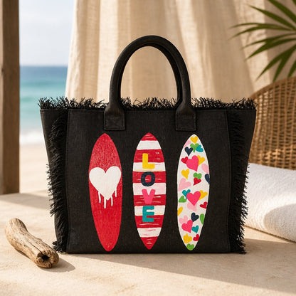 Hand-painted black fringed tote bag featuring three colorful surfboards with heart designs and the word “LOVE,” set against a neutral background.