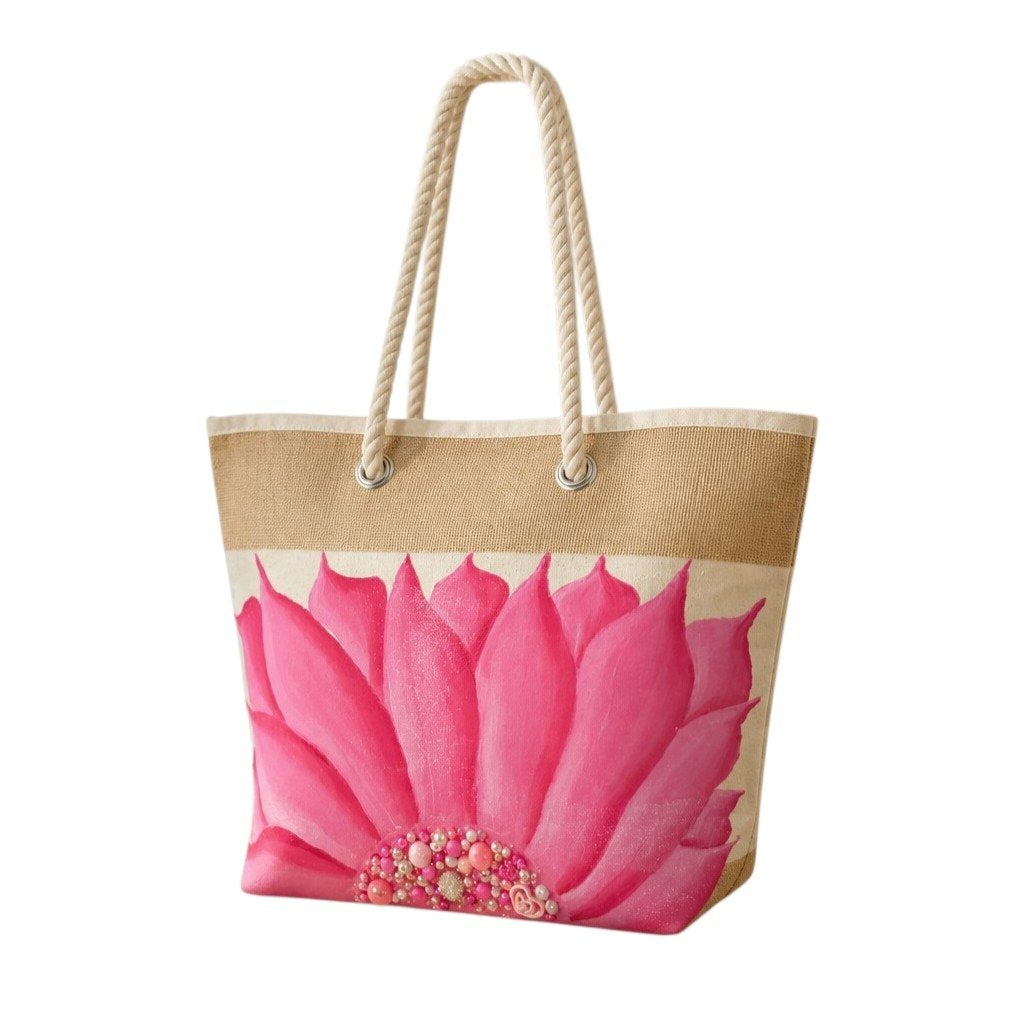 Hand-painted rope handle beach tote featuring a bold pink floral design with jeweled embellishments at the flower center, accented with natural jute trim and oversized cream rope handles against a neutral background.