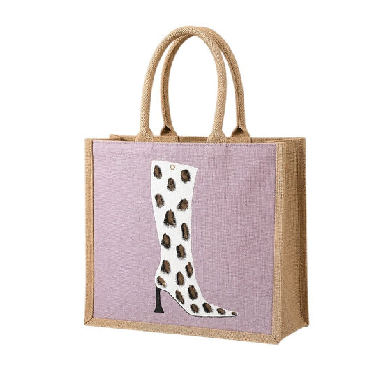 Hand-painted pink jute tote bag featuring a white cow-print western boot design with black and brown spotted detailing, inspired by modern western fashion and wearable art styling.