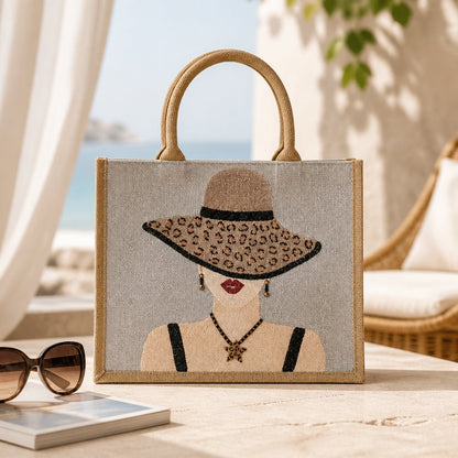 Hand-painted neutral jute tote bag featuring a stylish woman in a leopard-print sun hat with black straps, red lips, statement earrings, and natural woven handles.