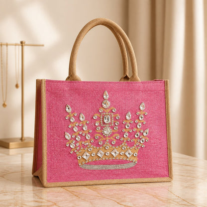 Hand-painted pink jute tote bag featuring an embellished gold crown design with sparkling rhinestones and jewel accents, finished with natural burlap handles and sides.
