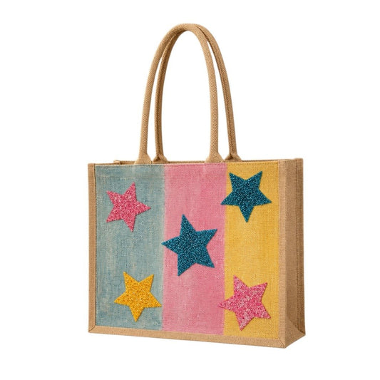 Colorful hand-painted jute tote bag featuring pastel blue, pink, and yellow panels accented with glittery star designs in teal, pink, and gold. The structured tote has natural woven handles and a bright, playful aesthetic inspired by fun artisan fashion accessories.