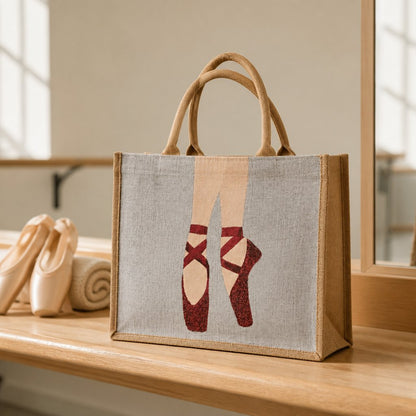 Hand-painted jute tote bag featuring elegant red ballet pointe shoes on a soft neutral background. This dance-inspired tote combines natural woven textures with graceful ballet imagery, creating a stylish and artistic accessory for dancers and ballet lovers.